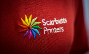Image of the Scarbutts logo embroidered onto a red polo shirt